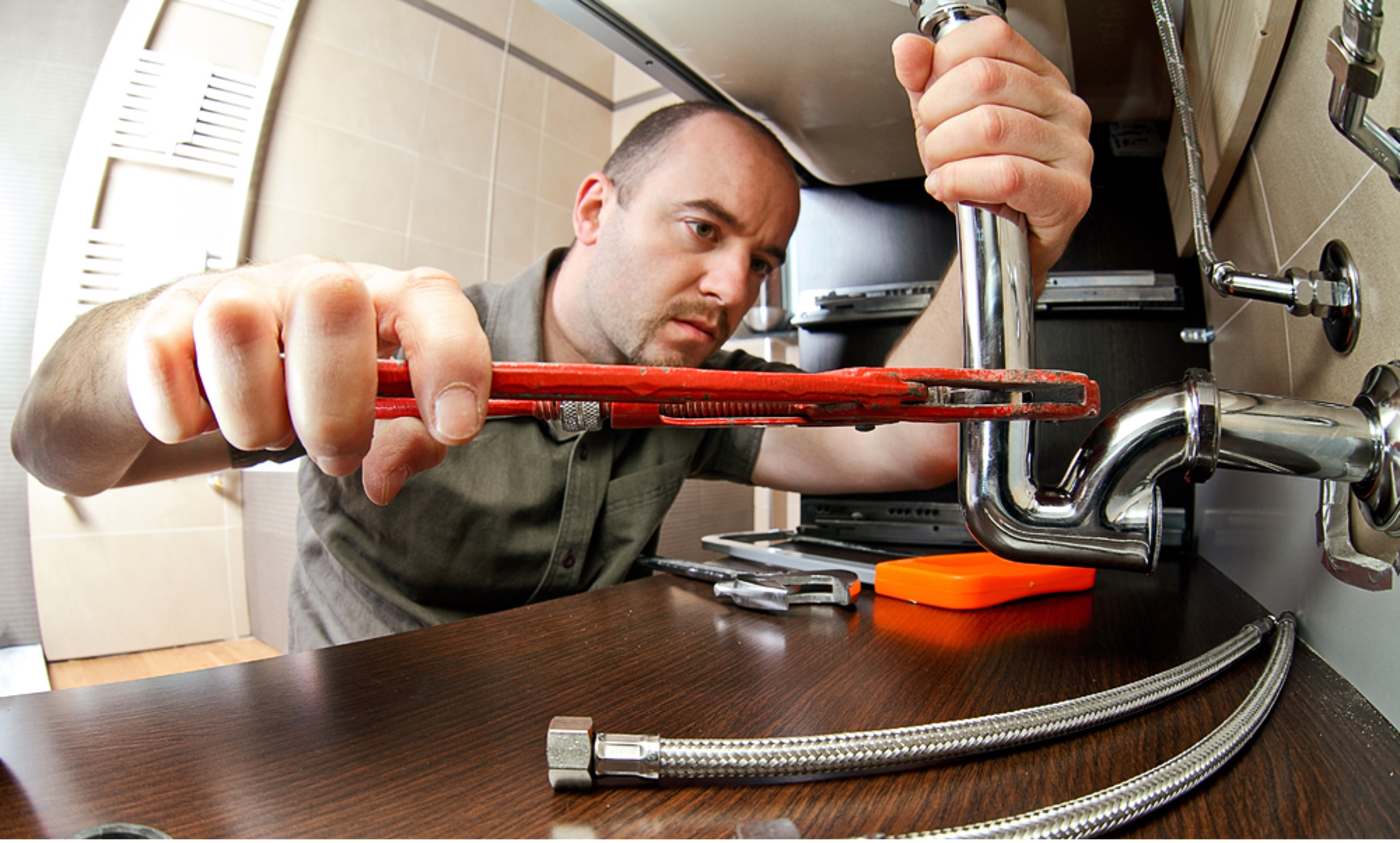 Plumber with pipe wrench under sink
